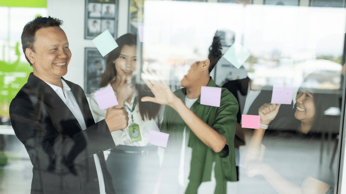 Business team smiling and organizing colorful sticky notes on a glass wall during a creative planning session in the office